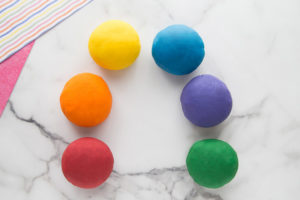 Red, orange, yellow, blue, purple, and green playdough balls arranged in a semi-circle