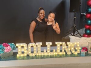 mother and daughter stand behind a celebratory sign saying Bolling, their last name